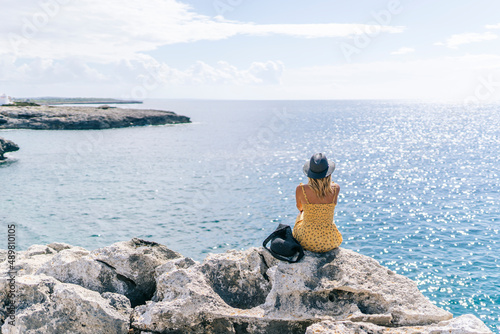 Woman sitting on rock looking at seascape on sunny day, Minorca, Spain photo