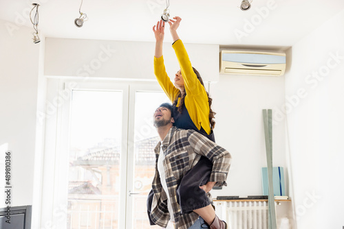 Young woman changing light bulb on boyfriend's back and renovating home photo