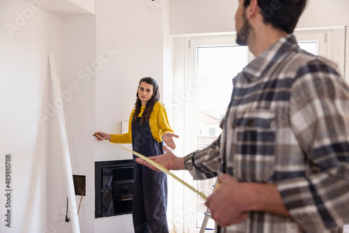 Confused woman with measuring tape talking with boyfriend in new living room