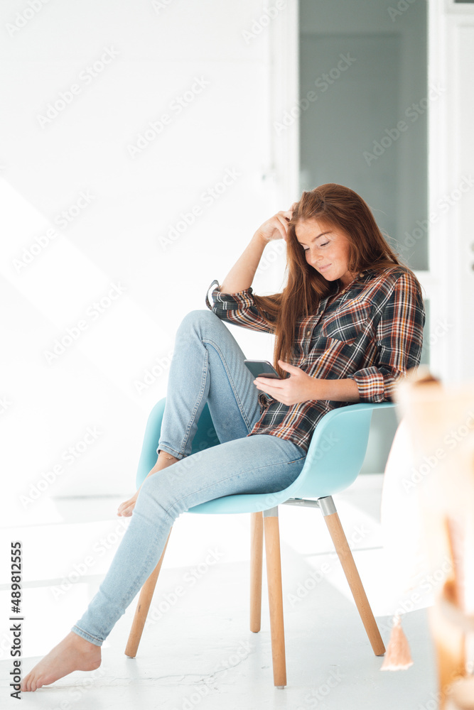 Young woman using smart phone sitting on chair at home Young woman using smart phone sitting on chair at home