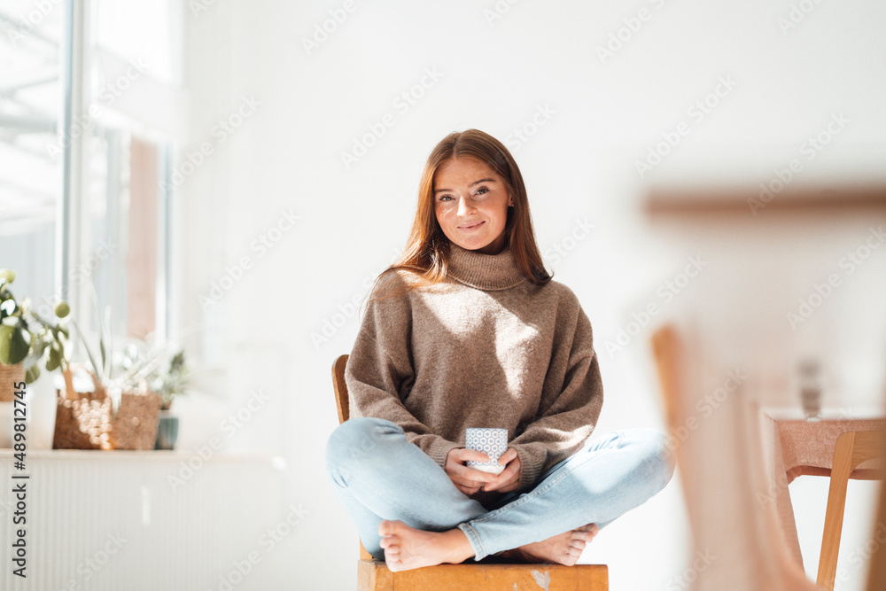 Smiling woman with coffee cup sitting on chair Smiling woman with coffee cup sitting on chair