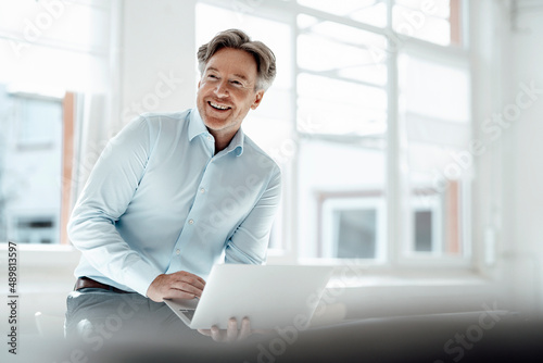 Smiling businessman with laptop in office photo