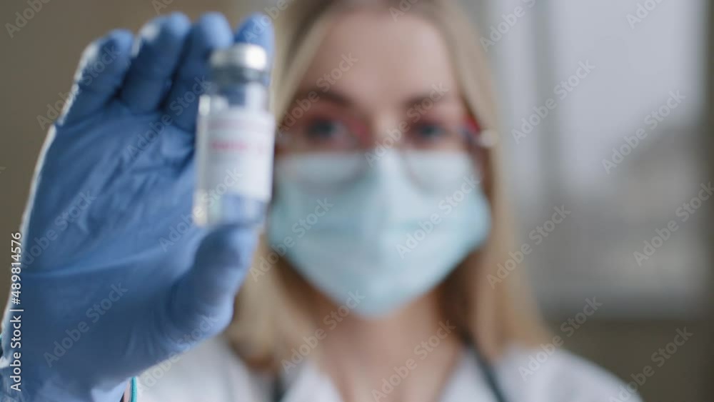 Close-up female specialist chemist biochemist woman doctor nurse scientist in medical mask glasses and latex gloves looking at camera holding bottle of covid vaccine coronavirus vaccination concept