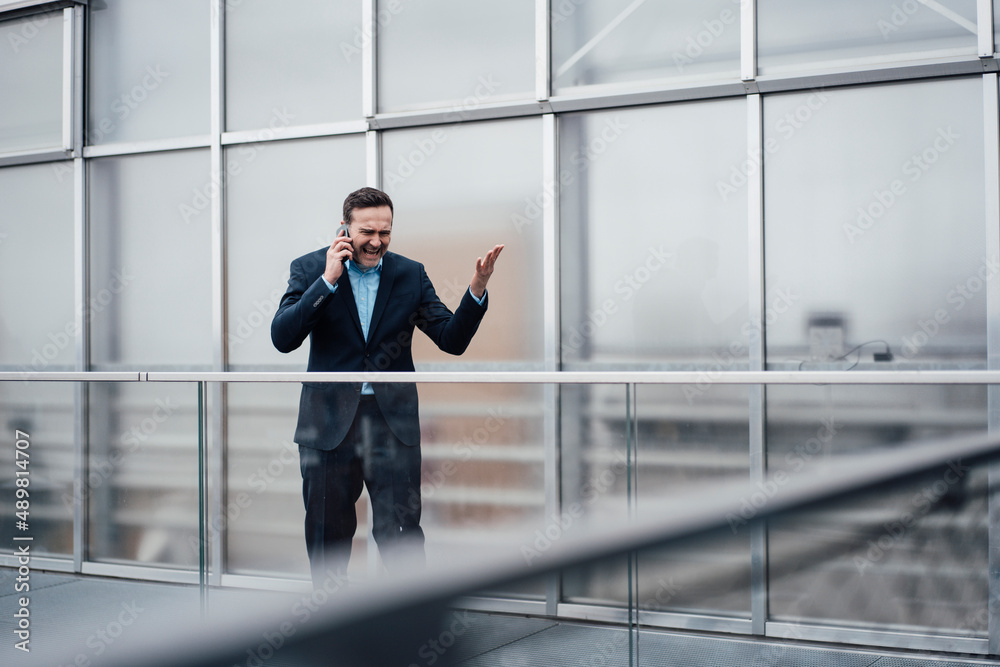 Frustrated businessman arguing on smart phone standing on balcony Frustrated businessman arguing on smart phone standing on balcony