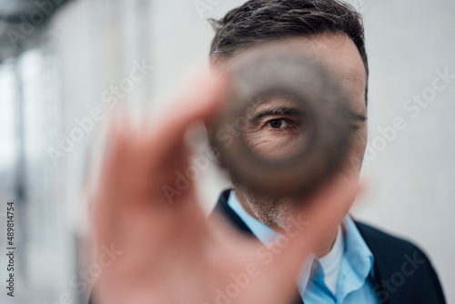 Businessman looking through cogwheel in greenhouse photo