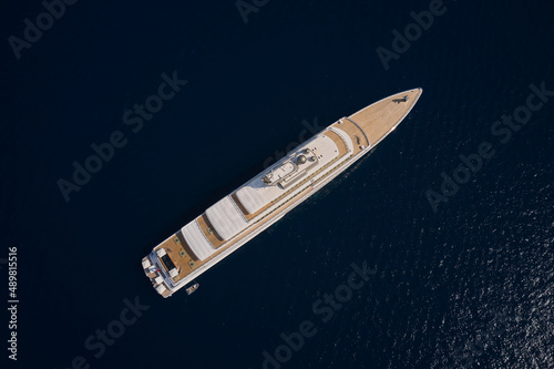 Big white super ship in the dark ocean aerial view. Luxurious white mega yacht on dark water in the reflection of the sun top view. Big yacht for millionaires in the sea drone view.