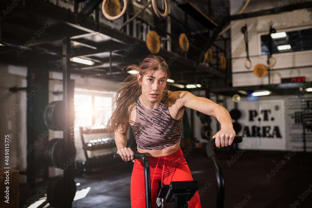 Attractive masculine young woman training on the bike in the modern interior gym testing her new gym equipment wearing sportswear. Fitness girl on her leg day in the sports center. Healthy lifestyle 