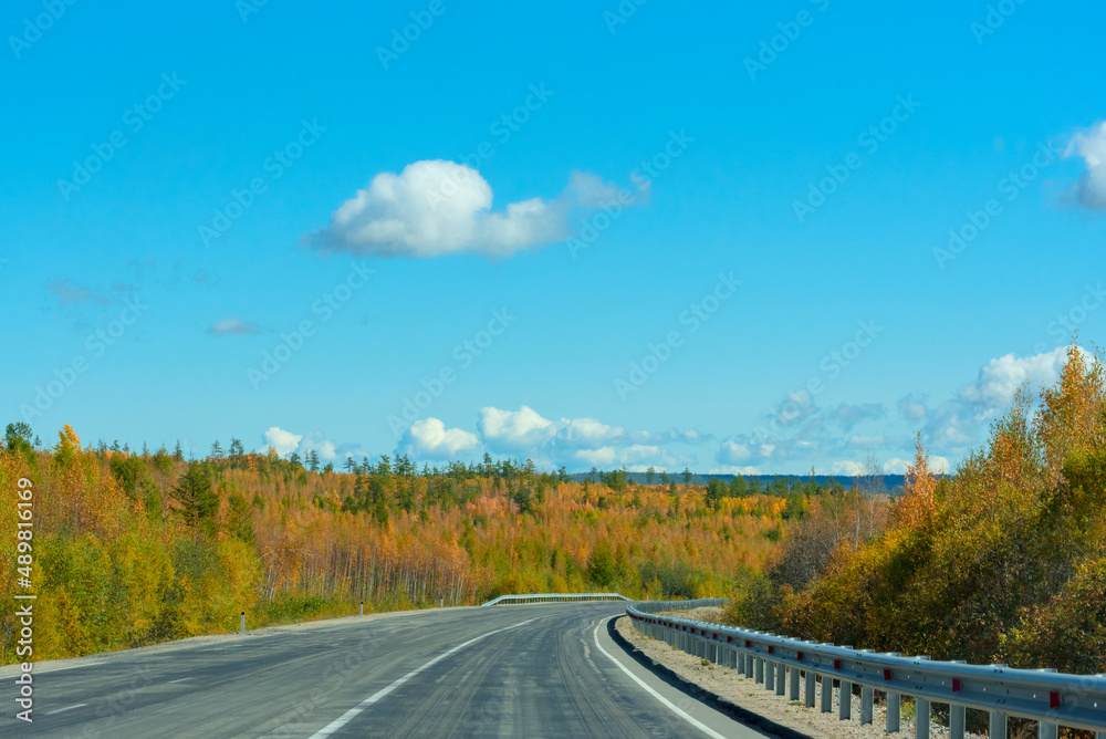 Bright autumn scene with road among orange and green trees and blue sky. Soft selective focus. Beauty of nature, travel concept