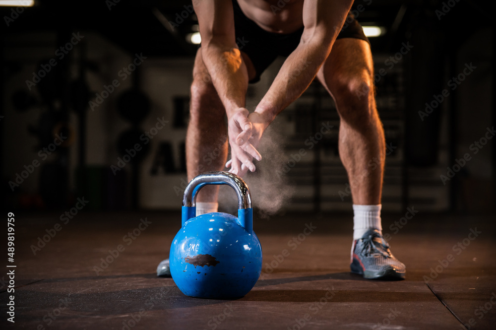 Naklejka premium Close up young masculine attractive bodybuilder man preparing to lift heavy weights for a full body cardio excercise wearing sportswear and trainers in the modern enterior gym. Healthy lifestyle conce