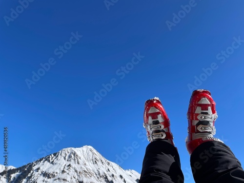 Woman's legs in red ski boots resting after a ski tour on sunny day, snowy Alps in the background. photo