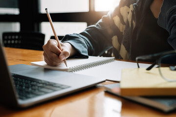 Cropped photo of asian woman writing making list taking notes in notepad working or learning on laptop indoors- educational course or training, seminar, education online concept