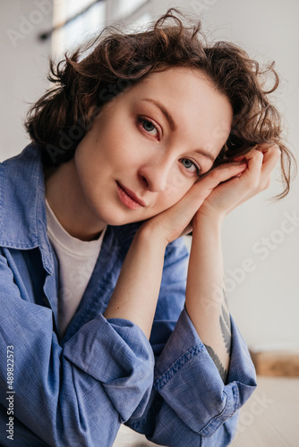 Close-up portrait of young woman with short curly hair in blue shirt looking at camera