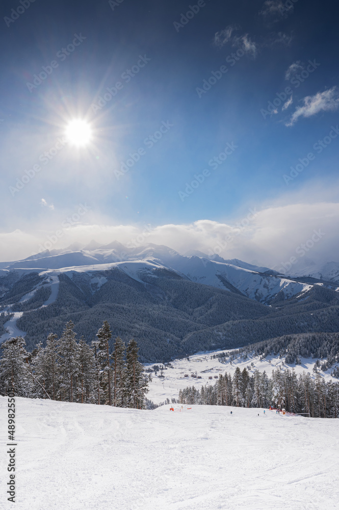 Beautiful landscape of the Arkhyz ski resort with mountains, snow, forest and track on a sunny winter day. Caucasus  Mountains, Russia. Vertical orientation