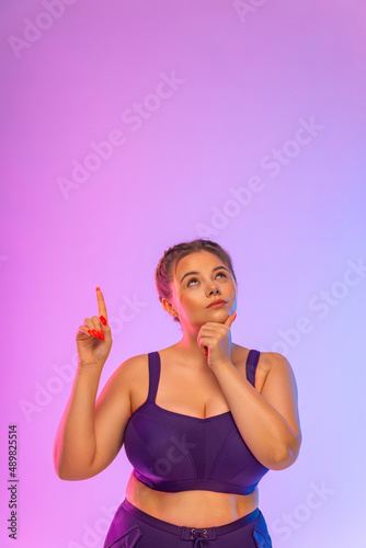 look up. Thoughtful woman standing isolated on pink background. Looking at the top and showing copyspace. Girl pointing on copy space.