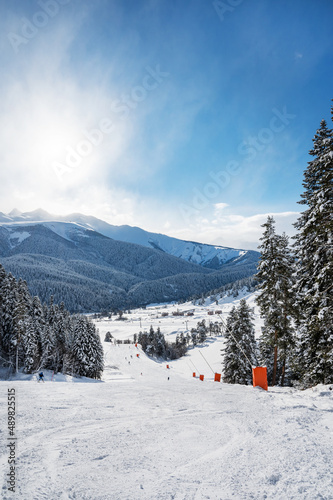 Beautiful landscape of the Arkhyz ski resort with mountains, snow, forest and track on a sunny winter day. Caucasus Mountains, Russia. Vertical orientation