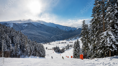 Beautiful landscape of the Arkhyz ski resort with mountains, snow, forest, skiers and snowboarders on a sunny winter day. Caucasus Mountains, Russia