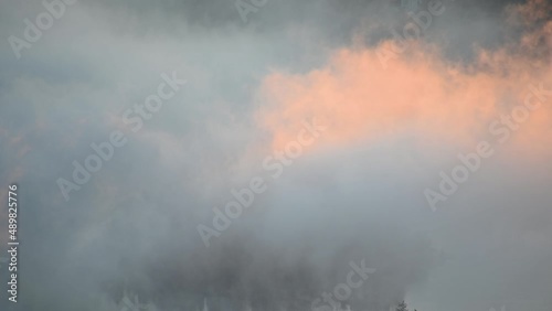 Elevated view of fog moving around small island on lake Bled, Slovenia. Aerial, telephoto perspective of sun illuminating low clouds. Fog or mist on the surface. Static shot, real time