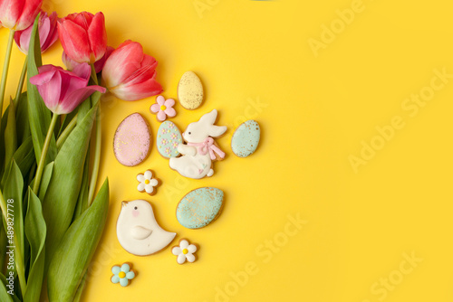 Happy Easter. Multi-colored pastel easter cookies gingerbread, seasonal flowers tulips on yellow background. Easter concept, copy space, flyer, banner, coupon, greeting card, invitation