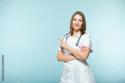 A beautiful female doctor with a stethoscope points to the place where there will be important information, on a blue background. Copy paste. healthcare concept.