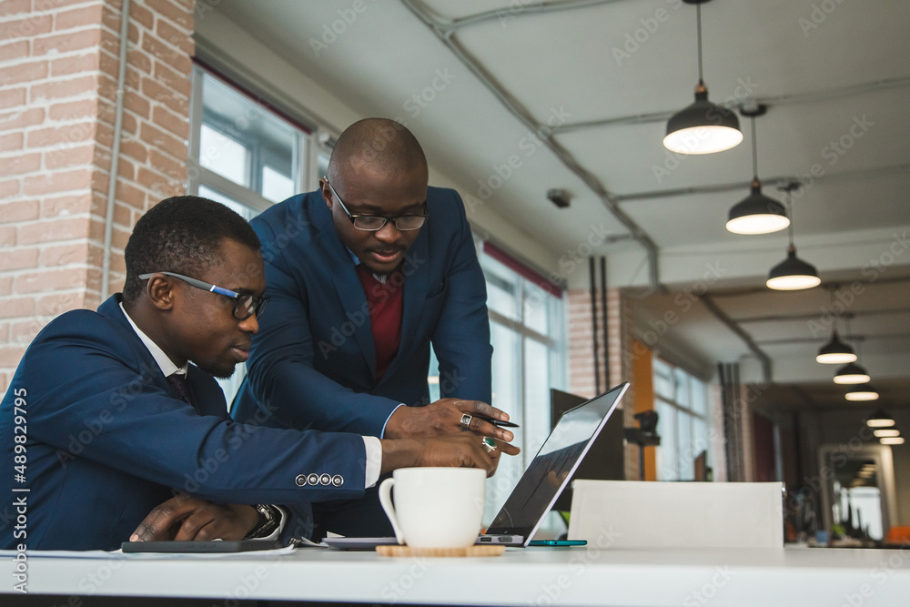 Two dark-skinned partners of an African American businessman in a meeting work on a laptop in the office. Affordable private courses and distance learning. New opportunities online Two dark-skinned partners of an African American businessman in a meeting work on a laptop in the office. Affordable private courses and distance learning. New opportunities online