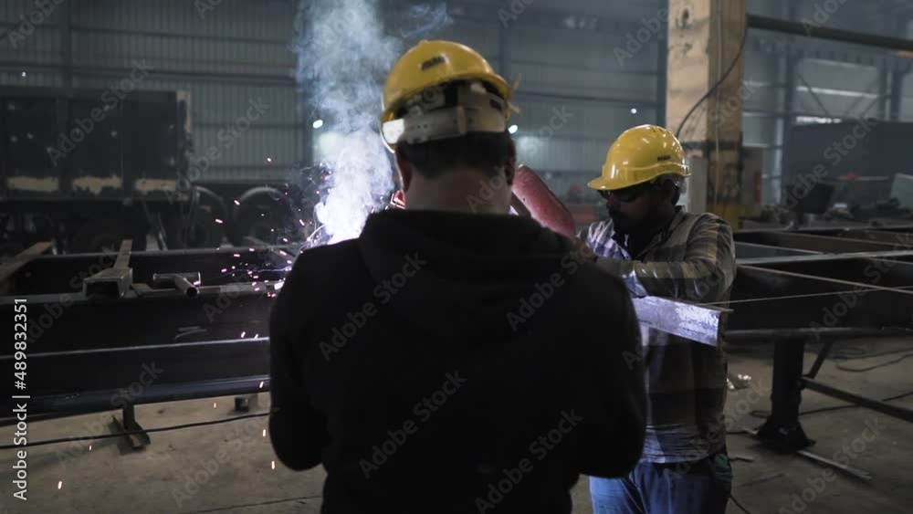 two Indian workers welding iron steel heavy metal in manufacturing production factory plant in India, technician team of working class people