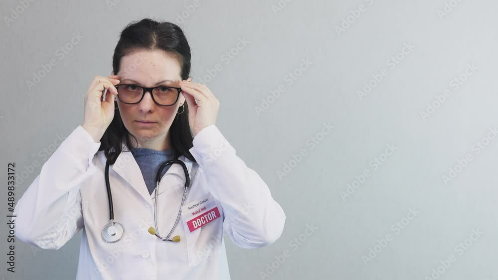 portrait brunette female doctor in white uniform coat lab with stethoscope around neck id badge identity taking off eye glasses from face, caucasian woman physician looking to camera, copy space grey portrait brunette female doctor in white uniform coat lab with stethoscope around neck id badge identity taking off eye glasses from face, caucasian woman physician looking to camera, copy space grey