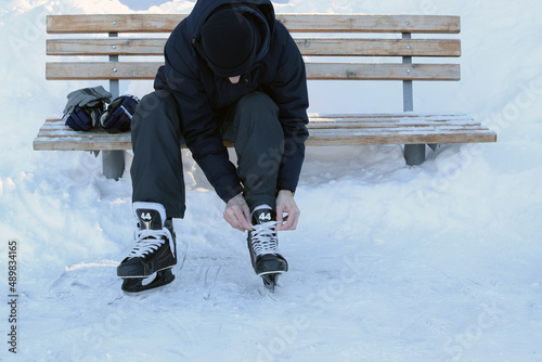 Man laces up hockey skates on an ice skating rink. Hockey gloves. Ice skating outdoors.
