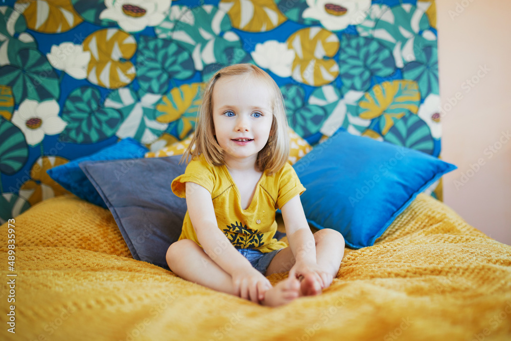 Adorable little girl sitting on bed in nicely decorated bedroom Adorable little girl sitting on bed in nicely decorated bedroom