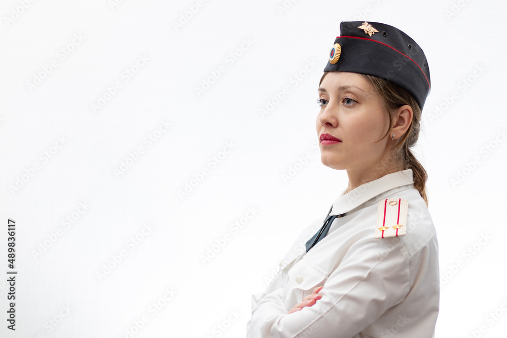 A beautiful young female Russian police officer in dress uniform in a cap and shoulder straps of a lieutenant colonel and a white shirt on a white background. Selective focus. Portrait A beautiful young female Russian police officer in dress uniform in a cap and shoulder straps of a lieutenant colonel and a white shirt on a white background. Selective focus. Portrait