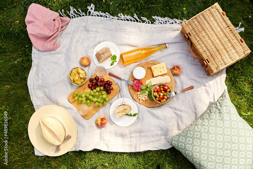 leisure and eating concept - close up of food, drinks and picnic basket on blanket on grass at summer park photo
