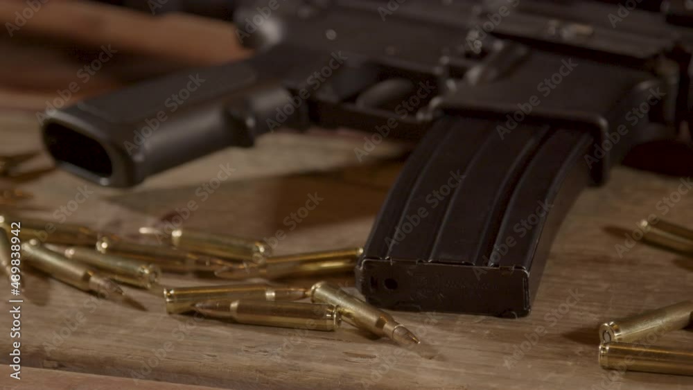 Close dolly out of AR-15 trigger and magazine with ammo scattered around on wooden surface Close dolly out of AR-15 trigger and magazine with ammo scattered around on wooden surface
