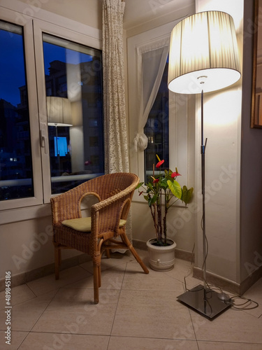 Home decor. Cozy corner with wicker armchair  potted flowers and lighted lamp.