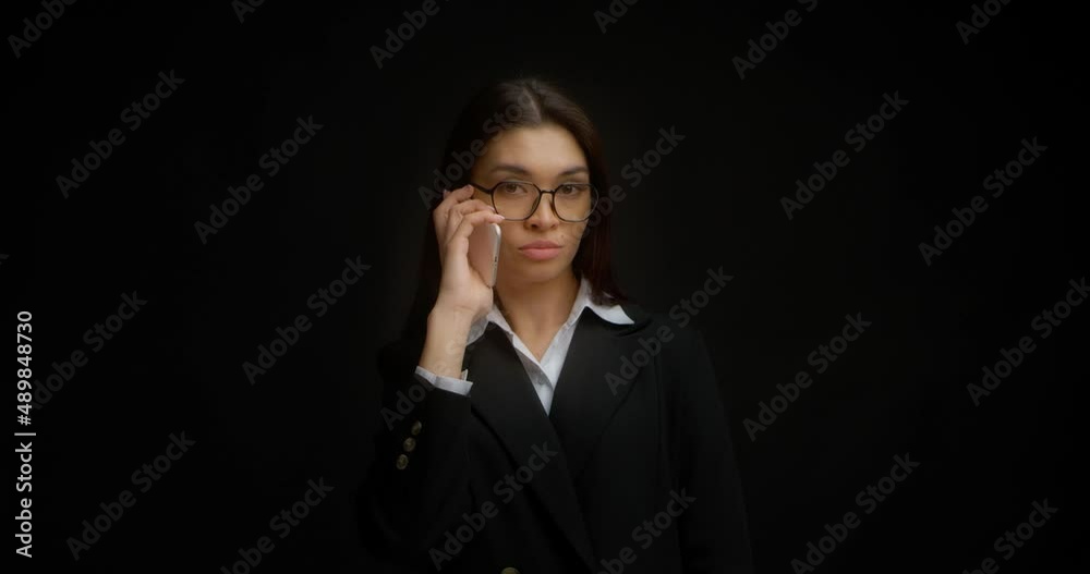 Businesswoman with glasses and a serious face is talking on the phone. Beautiful brunette in business clothes leads agrees with the interlocutor in negotiations on a smartphone Businesswoman with glasses and a serious face is talking on the phone. Beautiful brunette in business clothes leads agrees with the interlocutor in negotiations on a smartphone