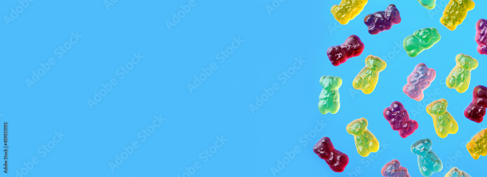 Multicolored flying gummy bears on blue background, flat lay. Banner