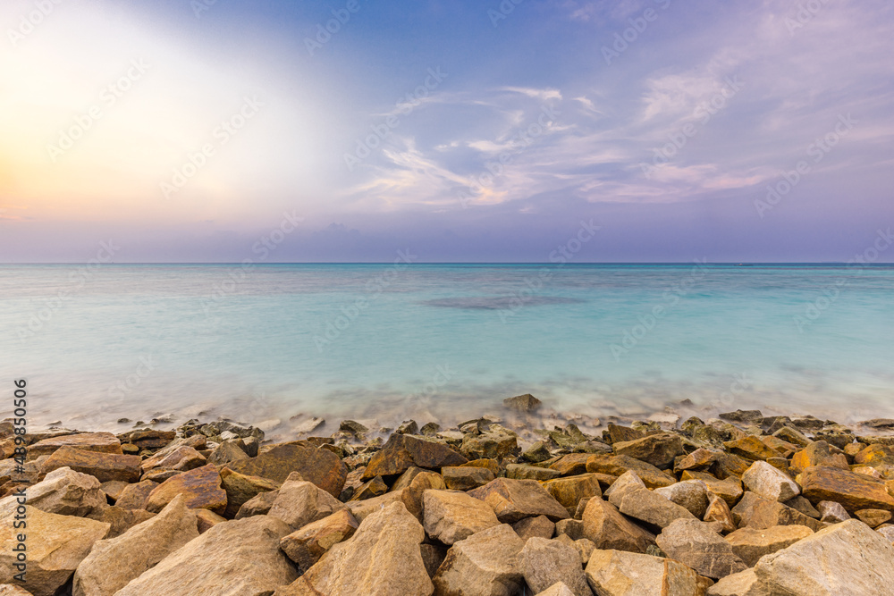 Tropical island view with beautiful sunset over the green boulders on a wave breaker. Rocks on exotic shore under colorful sky and horizon. Exotic sea, ocean lagoon artistic background concept Tropical island view with beautiful sunset over the green boulders on a wave breaker. Rocks on exotic shore under colorful sky and horizon. Exotic sea, ocean lagoon artistic background concept