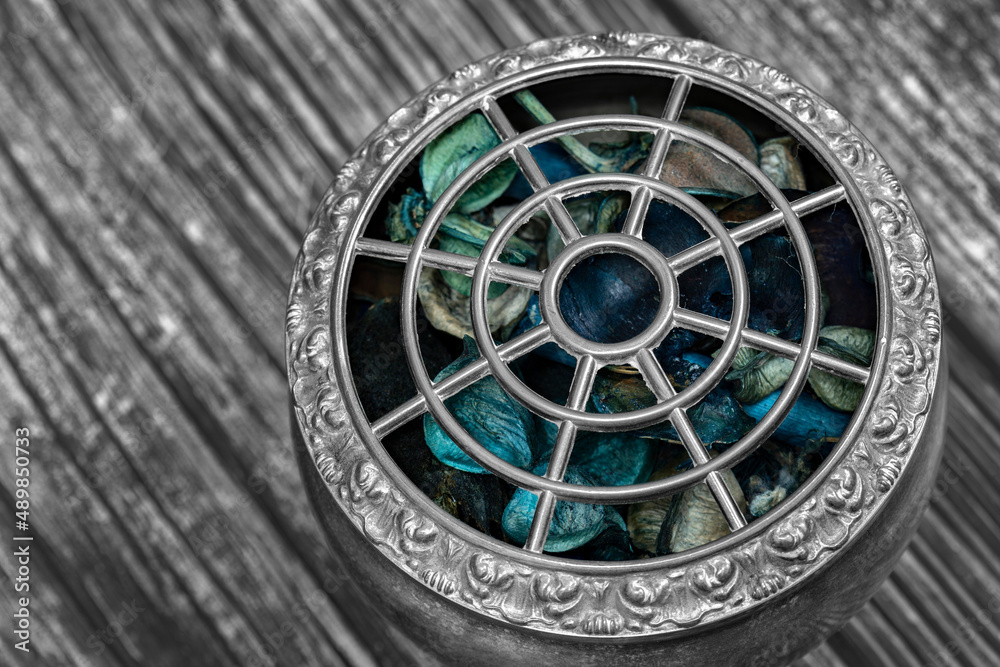 Potpourri in a vintage silver decorated bowl on a wood background.  With selective colour