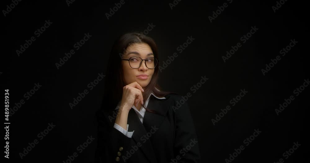 Business woman in glasses remembers and ponders a decision. A beautiful brunette in a black jacket came up with an idea. Isolated on black background Business woman in glasses remembers and ponders a decision. A beautiful brunette in a black jacket came up with an idea. Isolated on black background