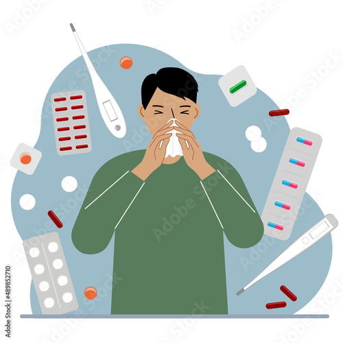 A man covers his nose with his hands with a handkerchief. The concept of a cold person, seasonal allergies. Lots of medicines and thermometers.
