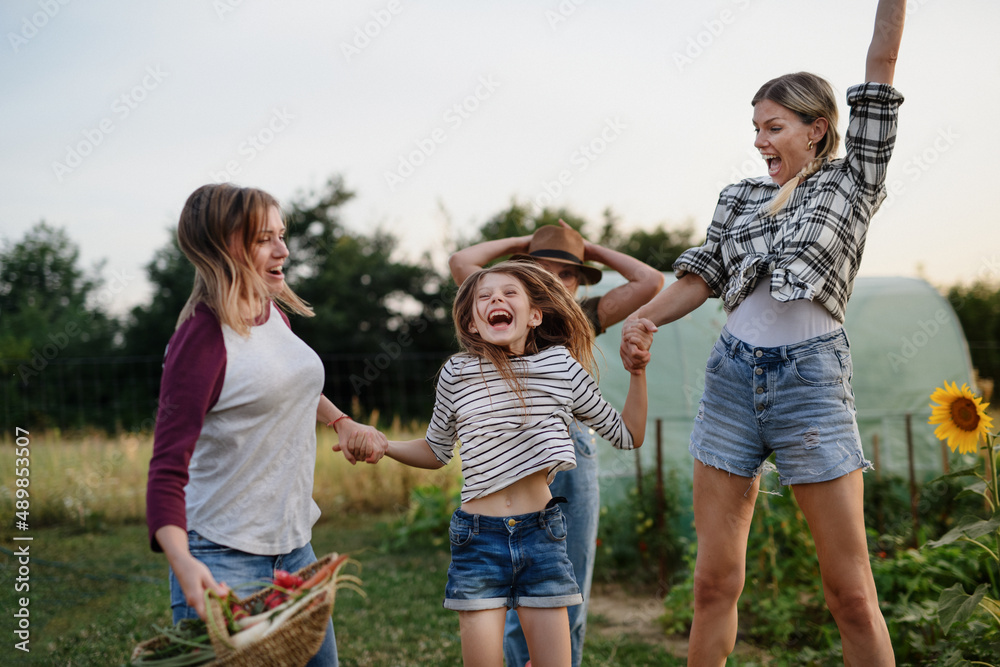Happy little girl with mother and aunt jumping outdoors at community farm.