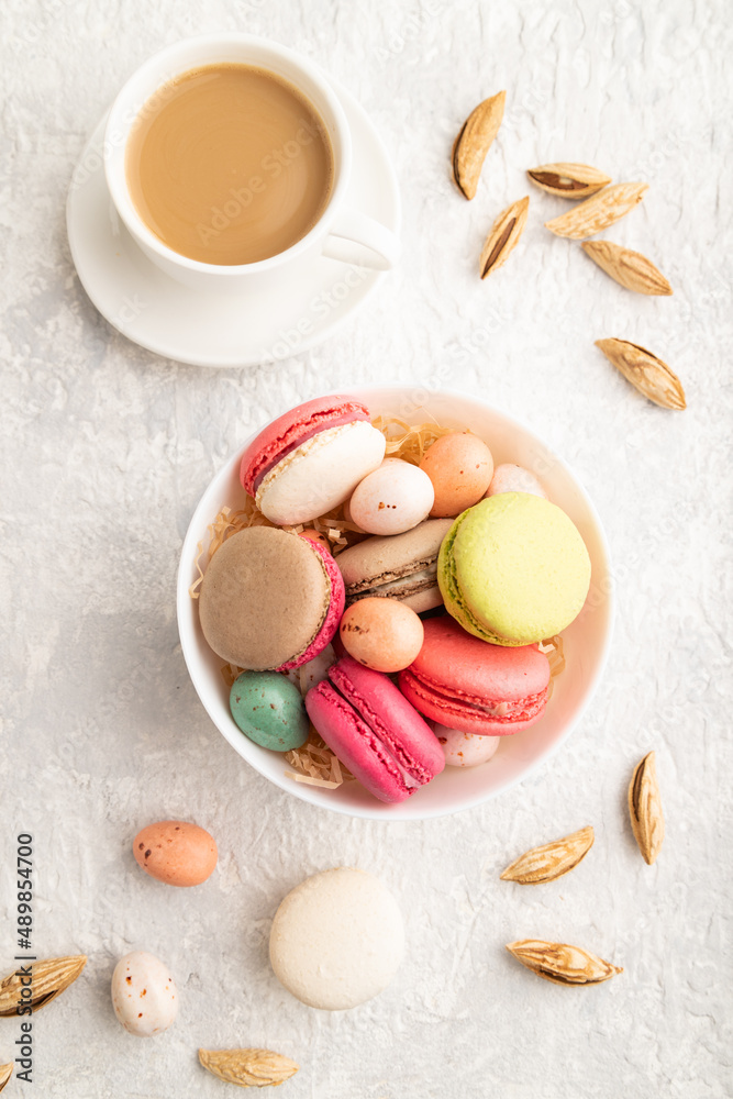 Different colors macaroons and chocolate eggs in ceramic bowl, cup of coffee on gray concrete background. top view, close up. Different colors macaroons and chocolate eggs in ceramic bowl, cup of coffee on gray concrete background. top view, close up.