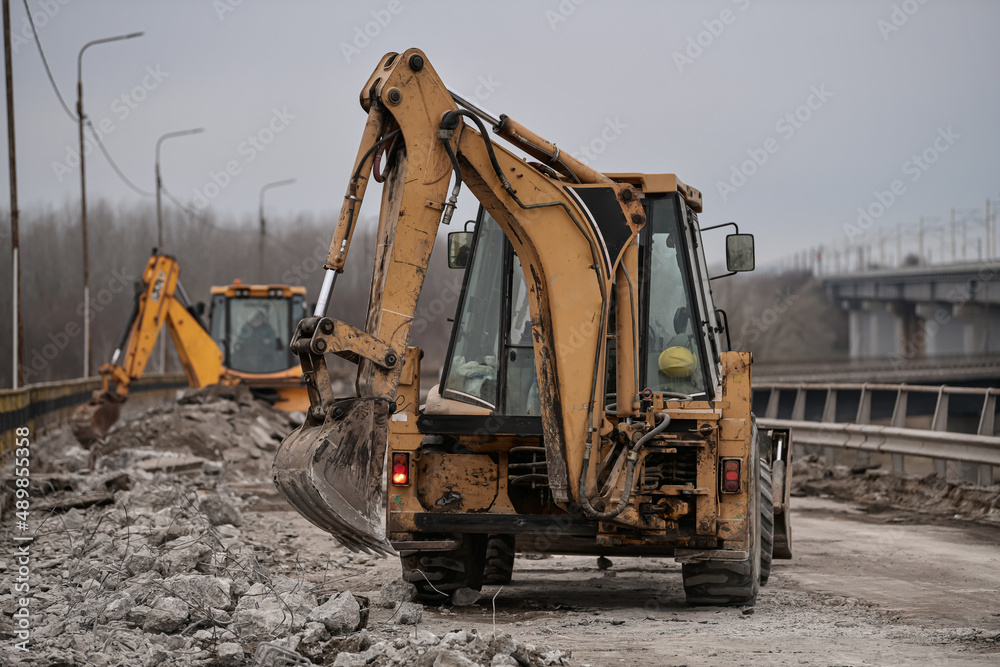 An excavator bulldozer truck working on a construction site for road asphalt renovation on a bridge. Demolition of the old layers of road. An excavator bulldozer truck working on a construction site for road asphalt renovation on a bridge. Demolition of the old layers of road.