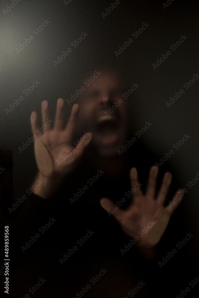 man with his hands on glass in front of his face screams in despair