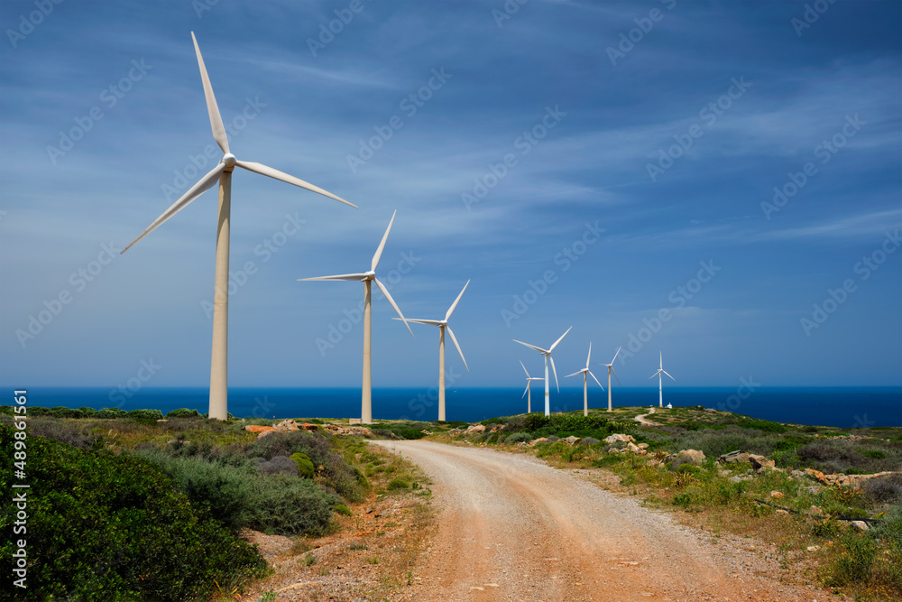 Green renewable alternative energy concept - wind generator turbines generating electricity. Wind farm on Crete island, Greece with road