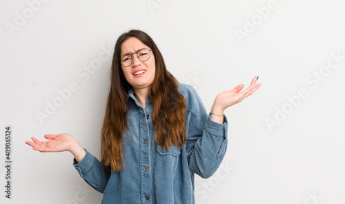 pretty caucasian woman shrugging with a dumb, crazy, confused, puzzled expression, feeling annoyed and clueless