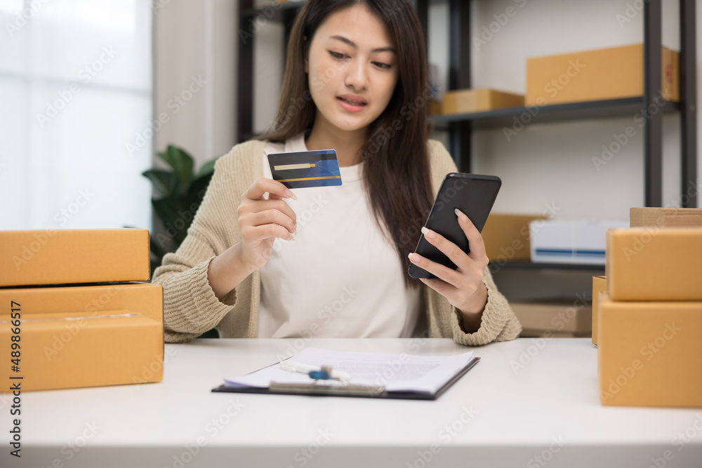 Shopping online. Young asian woman input the serial number of credit card to smartphone for shopping payment. Buying online at home. Small business entrepreneur with many parcel box on table Shopping online. Young asian woman input the serial number of credit card to smartphone for shopping payment. Buying online at home. Small business entrepreneur with many parcel box on table