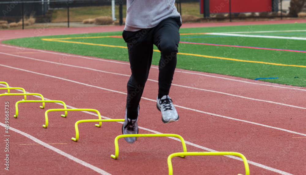 Fototapeta premium Runner in air over small plastic hurdels running a sports drill in lane on a track
