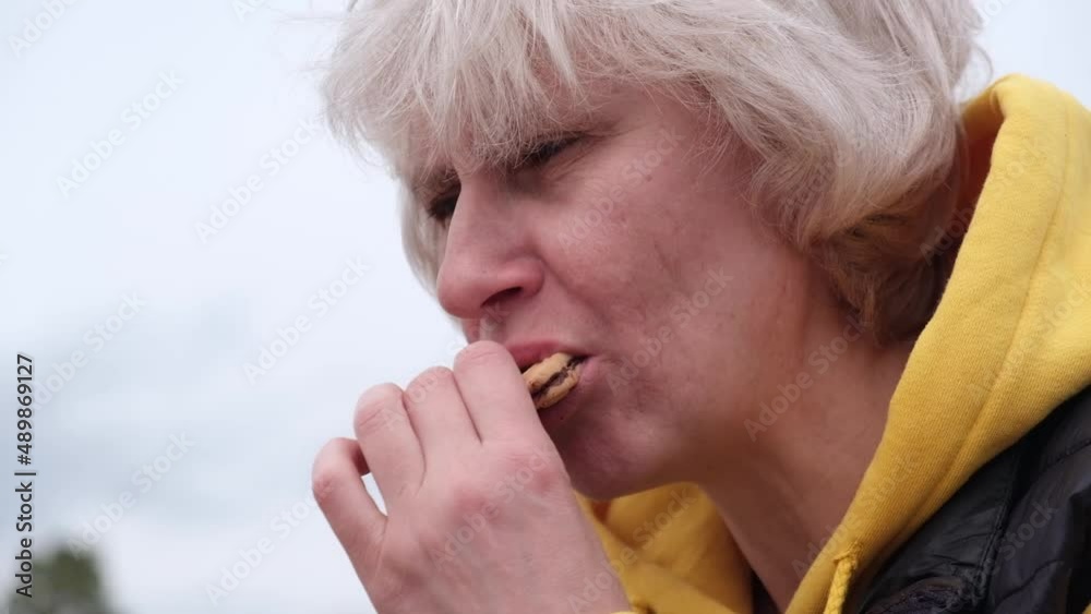 An attractive middle-aged female traveler eats cookies and drinks tea at a rest stop on a hike. Close-up. A woman takes a bite of cookies with pleasure and drinks tea or coffee from mug. Slow motion. An attractive middle-aged female traveler eats cookies and drinks tea at a rest stop on a hike. Close-up. A woman takes a bite of cookies with pleasure and drinks tea or coffee from mug. Slow motion.