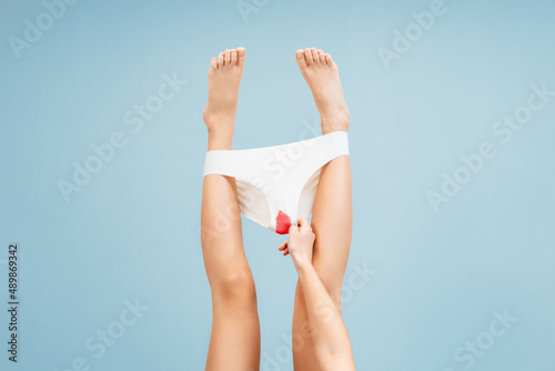 A woman holds her hand to her panties with a bloodstain. Blue background. Legs close-up. The concept of menstruation and gynecology photo