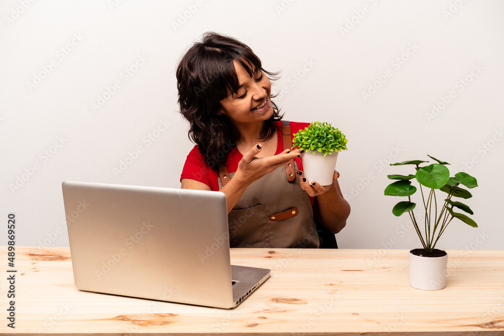Young gardener hispanic woman sitting on a table isolated on white background Young gardener hispanic woman sitting on a table isolated on white background