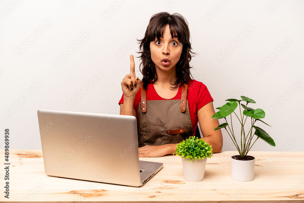 Young gardener hispanic woman sitting on a table isolated on white background having some great idea, concept of creativity. Young gardener hispanic woman sitting on a table isolated on white background having some great idea, concept of creativity.
